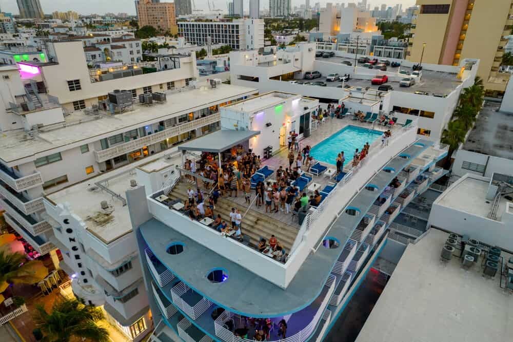 Aerial view of a rooftop pool party at a city hotel, popular among guests seeking the best swinger resorts Florida has to offer; people gather around the pool and seating area, with city buildings visible in the background.