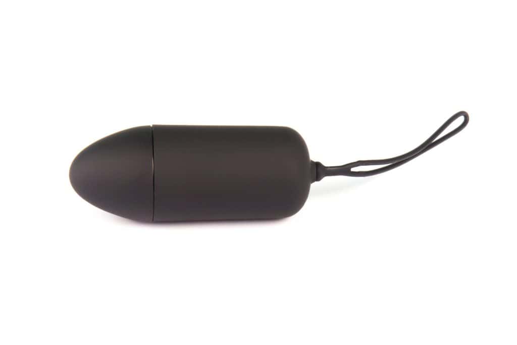 A small, black, cylindrical remote control vibrator hotwife toy with a tapered end and wrist strap, placed on a white background.