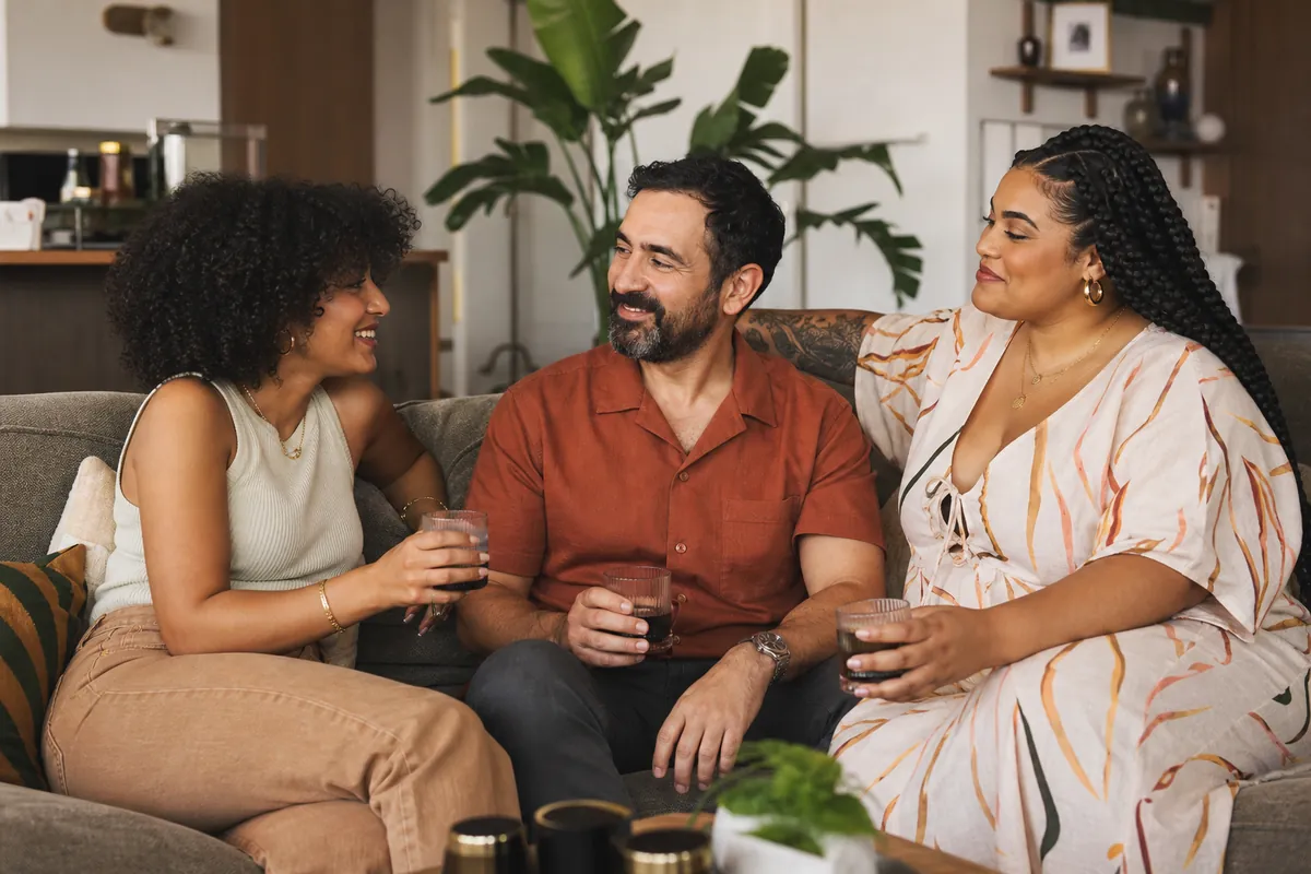 Three people share an intimate and connected conversation in a comfortable setting, representing the importance of inclusion and communication in threesome dynamics.