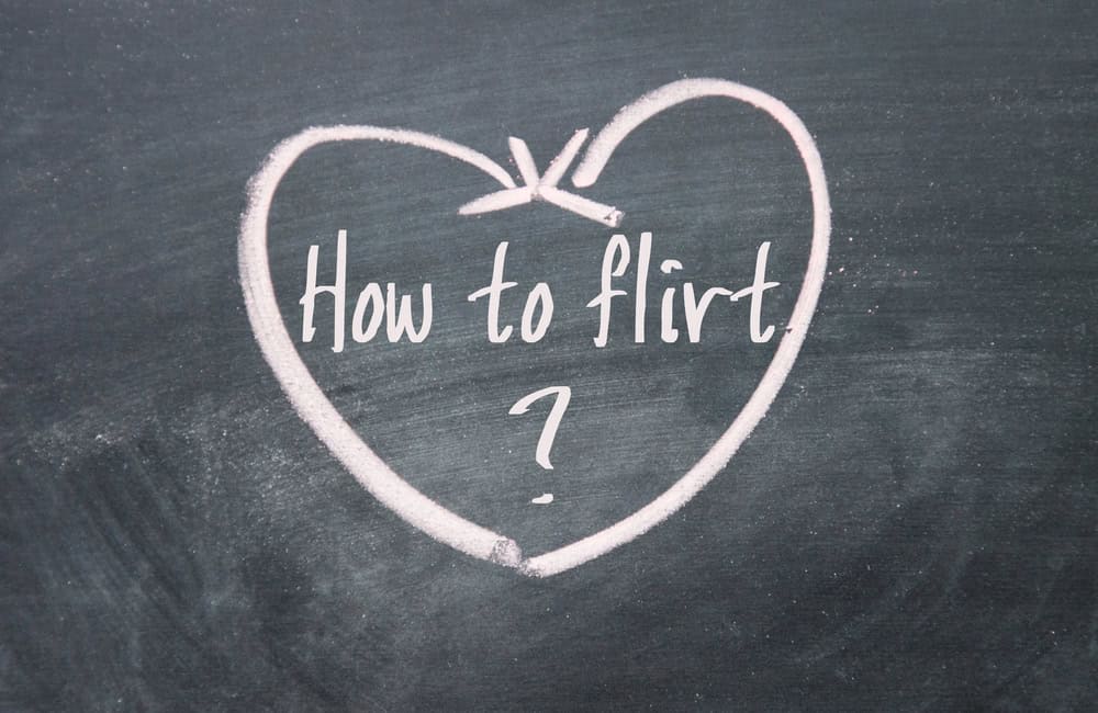 The phrase "How to flirt?" is written inside a heart drawn with pink chalk on a blackboard—a charming nod to flirting without pressure.