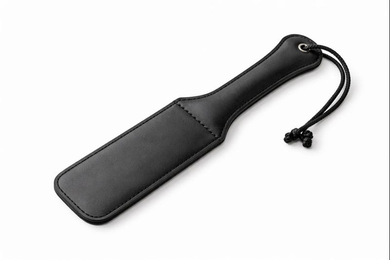A black leather paddle with stitching and a looped string handle, placed on a white background—perfect for those exploring impact play basics.